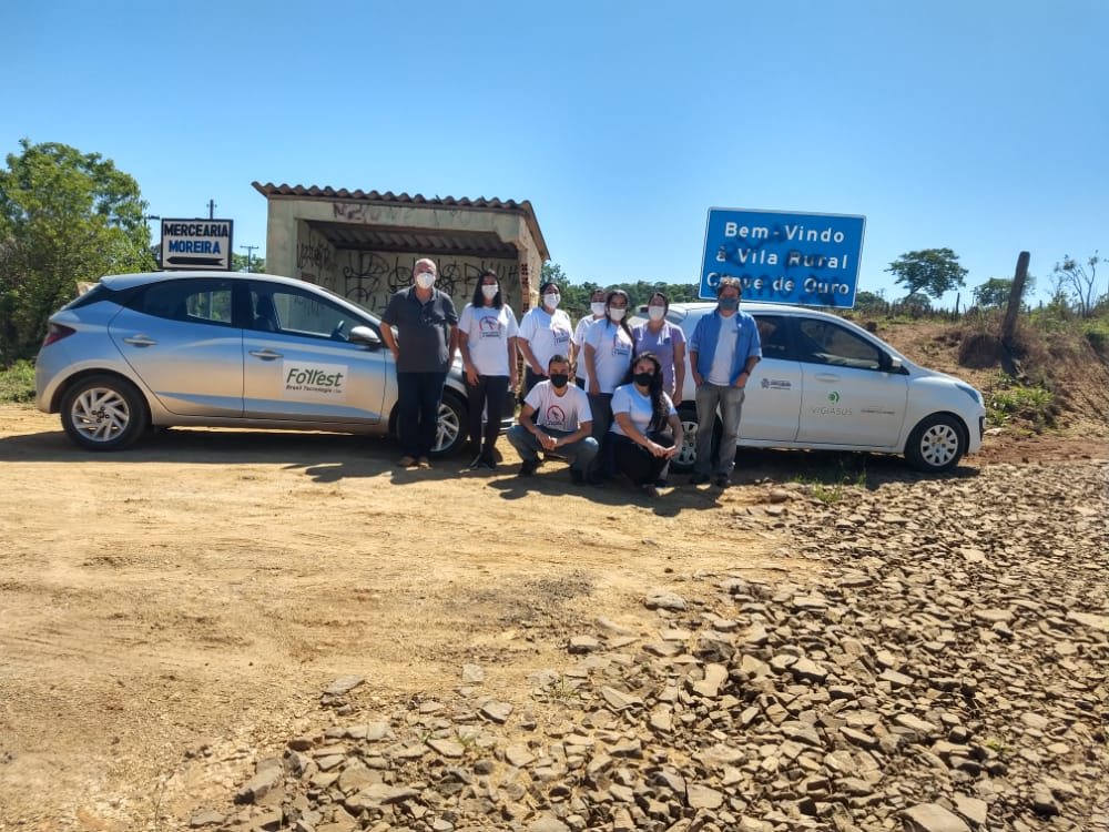 Equipe reunida ao lado dos veículos, na entrada de uma vila rural